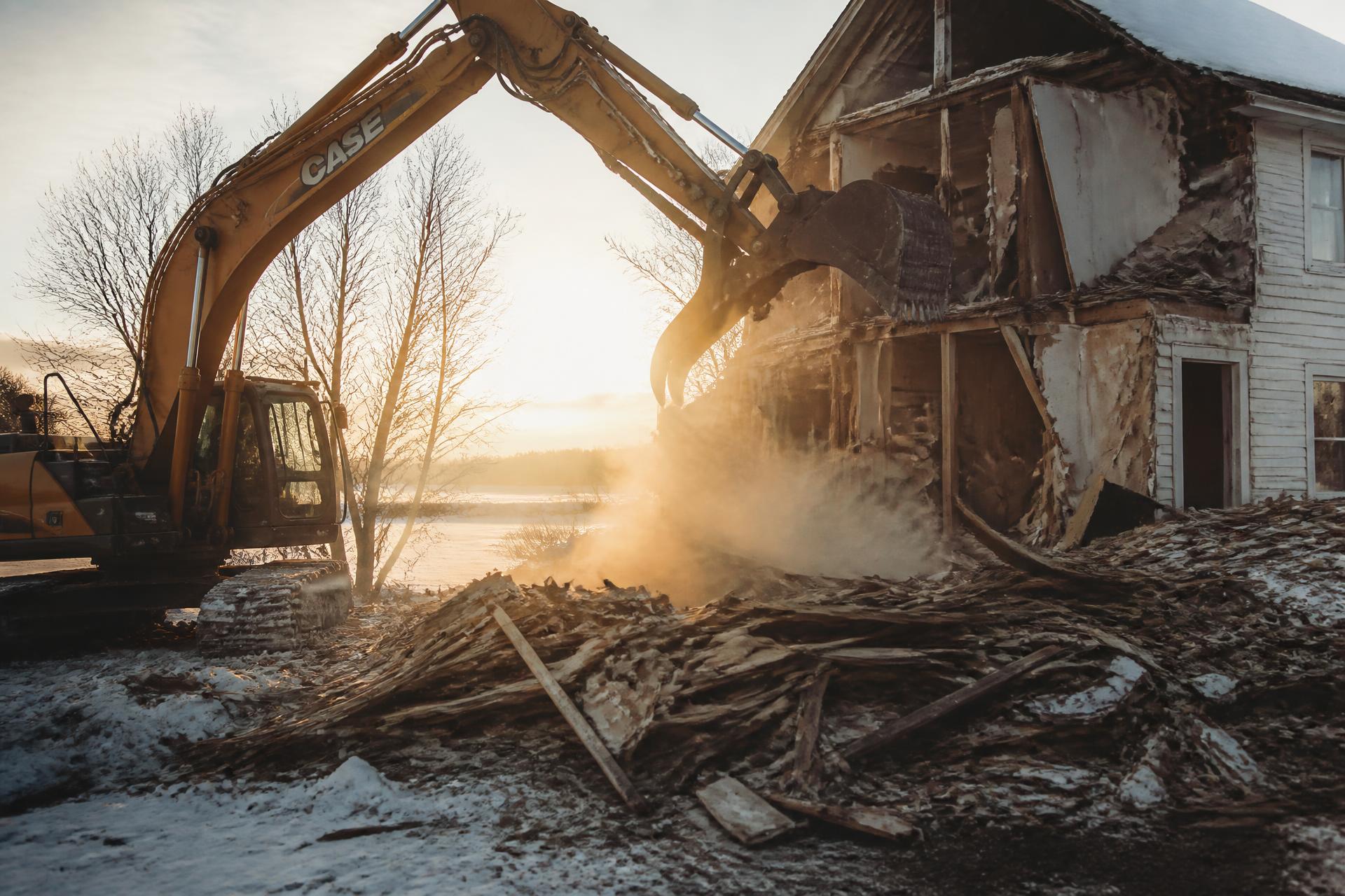 A residential structure being pulled apart by an excavator in winter