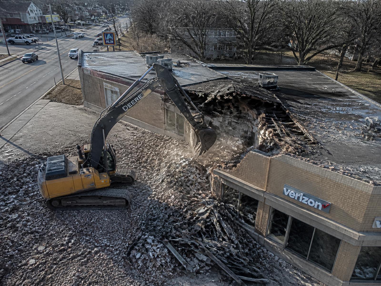 Aerial view of a tracked excavator opening the roof of a small commercial storefront