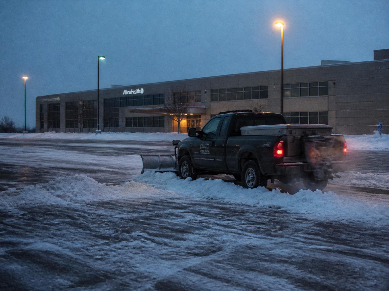 Pickup truck with a plow clearing a medical office parking lot at dawn